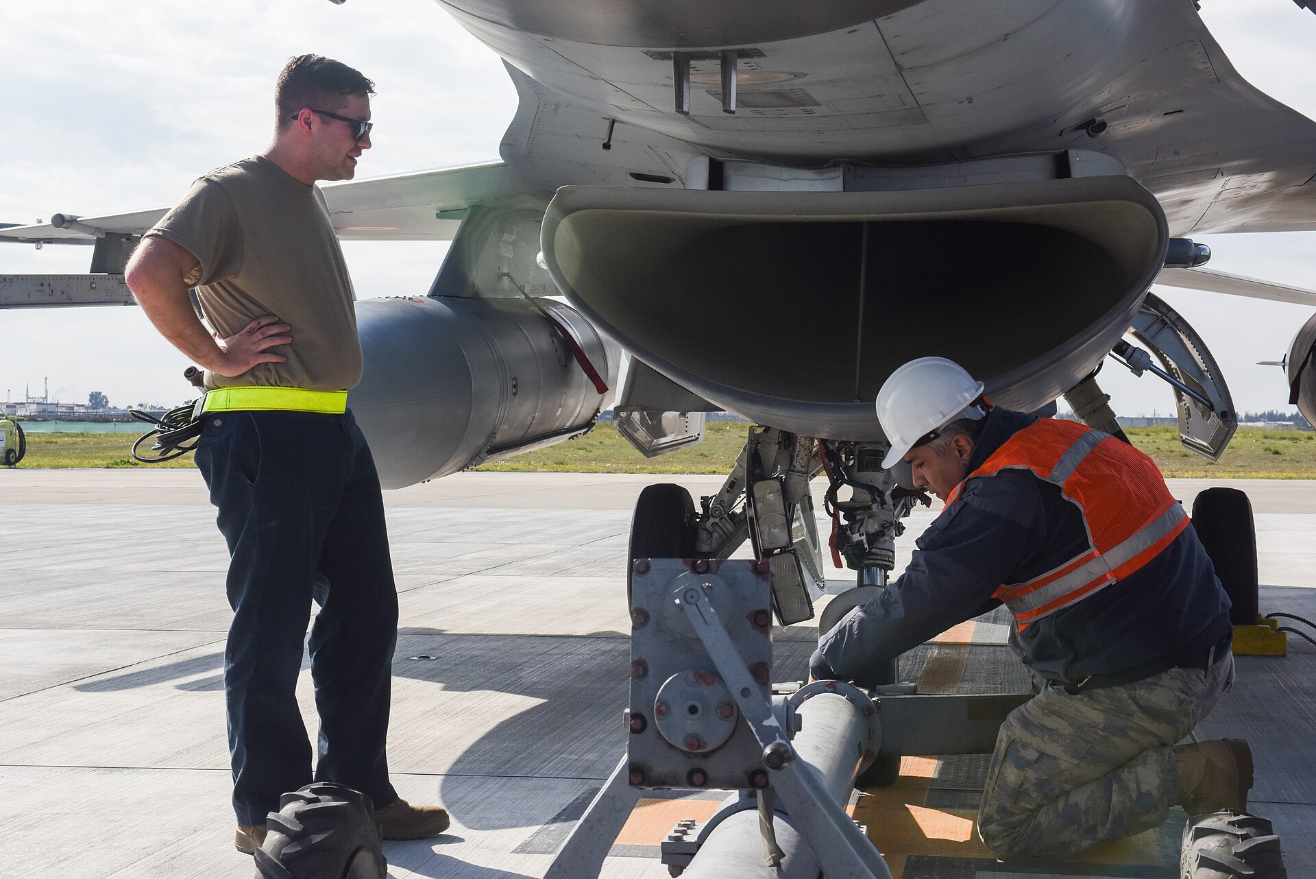 F-16'nın altında kaldırma ekipmanı kuran baretli bakım teknisyeni